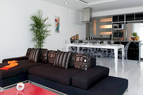 Modernes Wohnzimmer des Grand Sirenis Riviera Maya Resort mit schwarzem Sofa, weißem Esstisch und stilvoller Küche im Hintergrund.