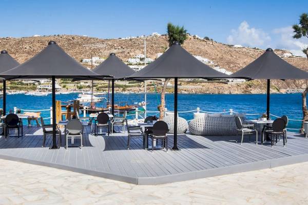 Strandterrasse des Kivotos Mykonos Hotels mit Tischen und Stühlen unter Schirmen