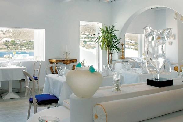 Innenansicht des Restaurants des Kivotos Mykonos Hotels mit weißen Tischen, Stühlen und Meerblick.