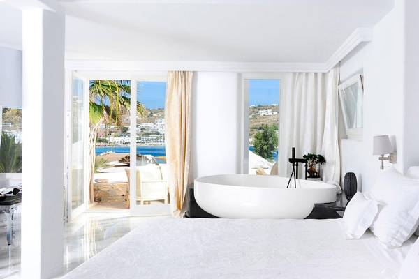 Schlafzimmer im Kivotos Mykonos Hotel mit Blick auf das Meer und einem großen Badewannenbereich.