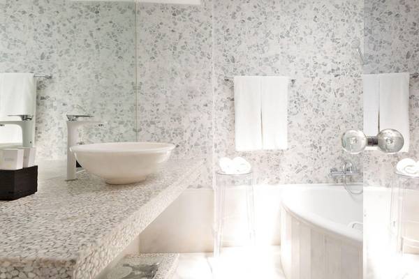 Das Badezimmer im Kivotos Mykonos Hotel mit mosaikartigen Wänden, weißen Möbeln und einem großen Badewannenbereich.