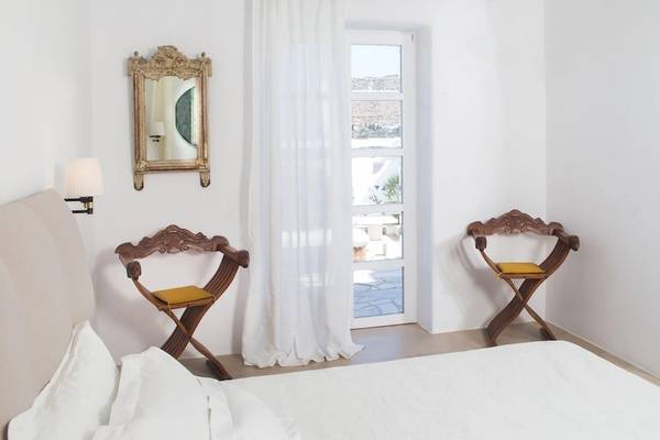 Innenansicht eines Zimmers im Kivotos Mykonos Hotel mit weißen Wänden, zwei Holzstühlen und einem Spiegel.