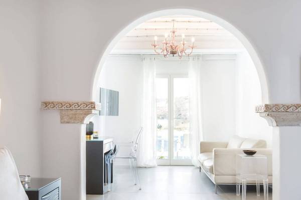 Weißes Wohnzimmer mit Couch, Schreibtisch, Kristallleuchte und Fenstern im Kivotos Mykonos.