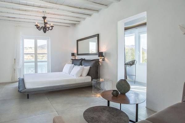 Innenansicht eines Zimmers im Kivotos Mykonos Hotel mit weißem Bett, Dekor und Möbeln.