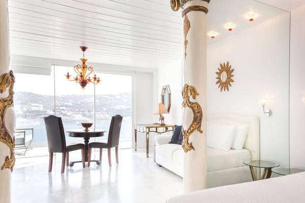Innenansicht eines Zimmers im Kivotos Mykonos Hotel mit weißer Einrichtung, großem Fenster und Meerblick.