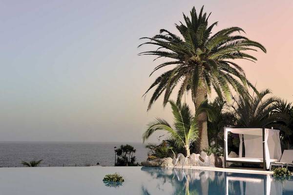 Ein Pool am Abend mit Blick auf das Meer und Palmen im Hintergrund.