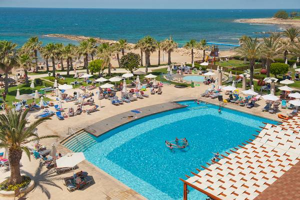 Überblick  über den Poolbereich des Louis Ledra Beach Hotels mit Sonnenliegen, Palmen und Meerblick.