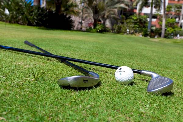 Golfschläger und Ball auf dem Rasen mit Gebäuden im Hintergrund