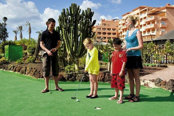 Familie spielt Golf im Elba Sara Beach & Golf Resort vor einem Gebäude mit vielen Balkonen.