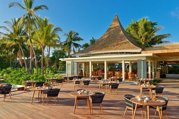Außenterrasse des Kuramathi Maldives Hotels mit runden Tischen und Stühlen unter Palmen