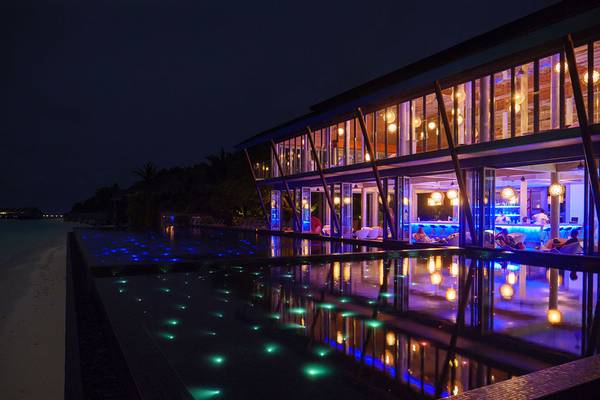 Nachtansicht des Kuramathi Maldives Hotels mit beleuchtetem Pool und Innenbereich.