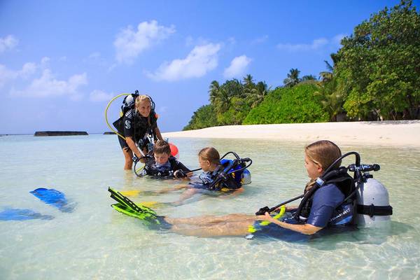 Familie beim Tauchen am Strand von Kuramathi Maldives, mit Tauchausrüstung und blauem Wasser