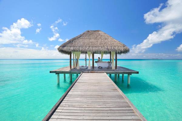 Strandhütte im Wasser mit Person auf Liege, blauer Himmel und Ozean