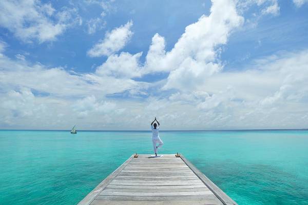 Eine Person praktiziert Yoga auf einem Pier im blauen Meer bei Kuramathi Maldives.