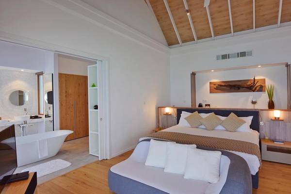 Schlafzimmer im Kuramathi Maldives Hotel mit Badewanne, Holzboden und weißen Wänden.