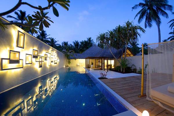 Außenbereich des Kuramathi Maldives Hotels bei Nacht mit beleuchtetem Pool und Liegestühlen.