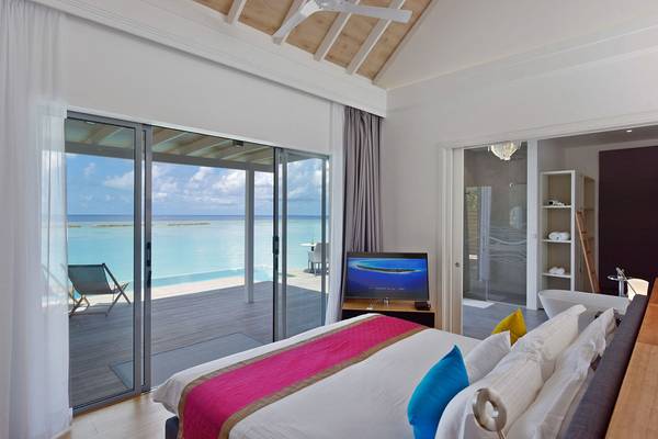 Schlafzimmer mit Meerblick im Kuramathi Maldives Hotel, mit Glastüren, Fernseher und bequemem Bett.