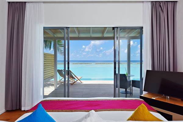 Zimmer mit Aussicht auf das Meer im Kuramathi Maldives, mit offenem Fenster, Loungestühlen und Fernseher.