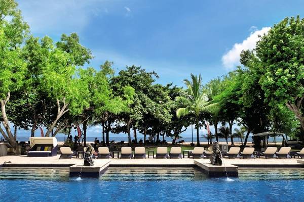 Außenpool des Mercure Resort Sanur mit Liegen und Bäumen im Hintergrund.