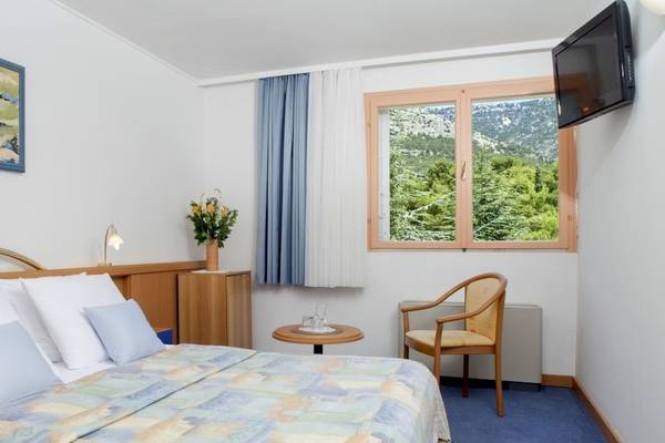 Zimmer im BlueSun Hotel Borak mit Bett, Tisch, Stuhl, Fernseher und Fenster mit Bergblick.