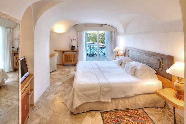 Schlafzimmer im Grand Hotel Poltu Quatu mit Doppelbett und Blick auf den Pool.