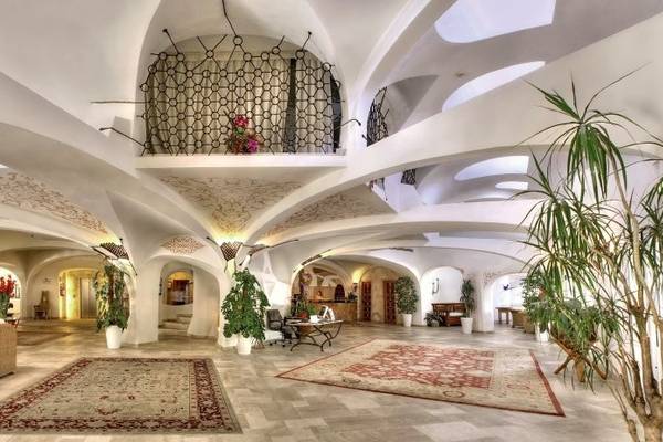Innenansicht der Lobby des Grand Hotel Poltu Quatu mit weißen Gewölbedecken, Teppichen und Pflanzen.