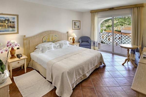 Schlafzimmer im Grand Hotel Poltu Quatu mit Bett, Nachttischen und Blick auf die Terrasse.