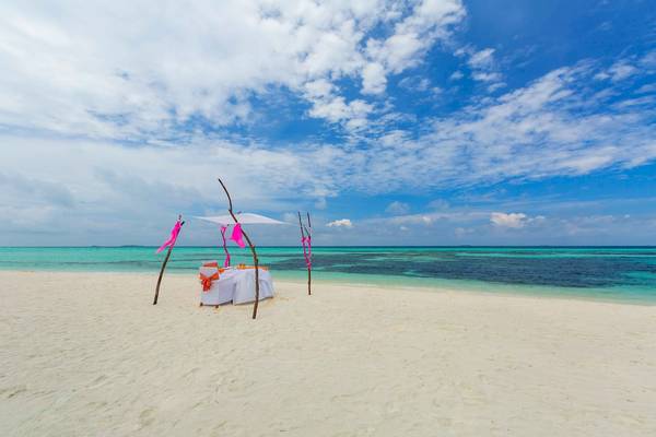 Hochzeitstisch auf dem Strand des Sun Siyam Olhuveli Hotels, bedeckt mit einem weißen Baldachin.