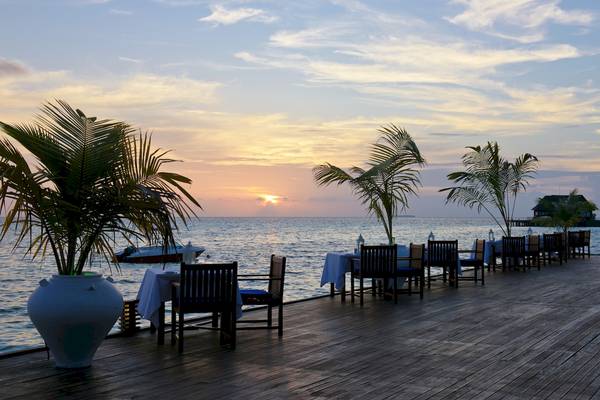 Sonnenuntergang am Strand des Sun Siyam Olhuveli mit Tischen und Stühlen am Meer.