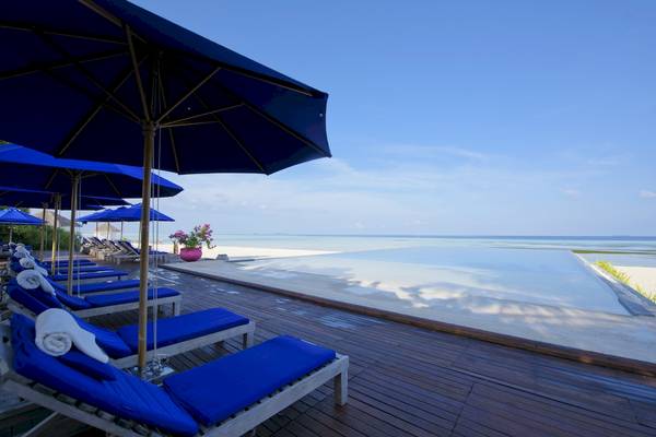 Terrasse des Sun Siyam Olhuveli Hotels mit blauen Liegen und Sonnenschirmen am Strand