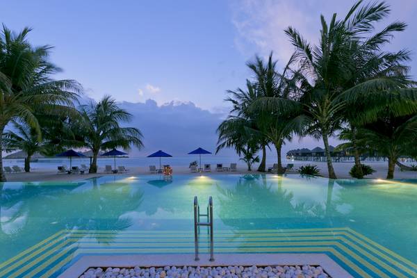 Schwimmbad am Abend im Sun Siyam Olhuveli Hotel mit Palmen und Sonnenschirmen.