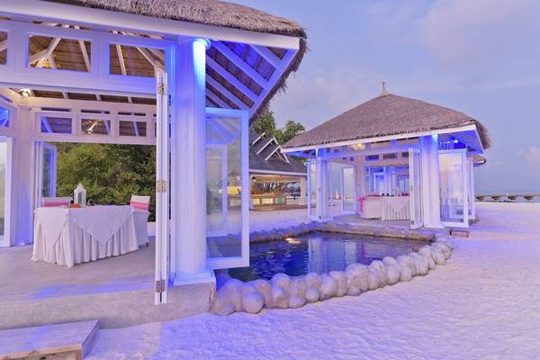 Strandhütte mit Tisch und Pool bei Sonnenuntergang im Sun Siyam Olhuveli Hotel.