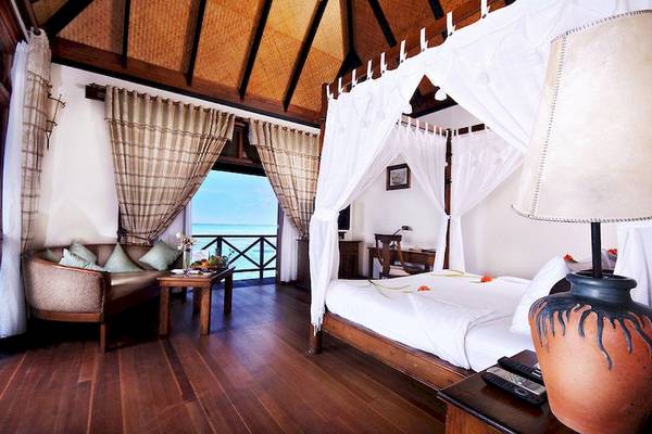 Hotelzimmer mit Bett, Tisch, Lampen und Blick aufs Meer im Sun Siyam Olhuveli
