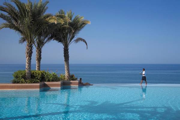 Ein Swimmingpool mit Blick auf das Meer, zwei Palmen und eine Person, die einen Tablett hält.