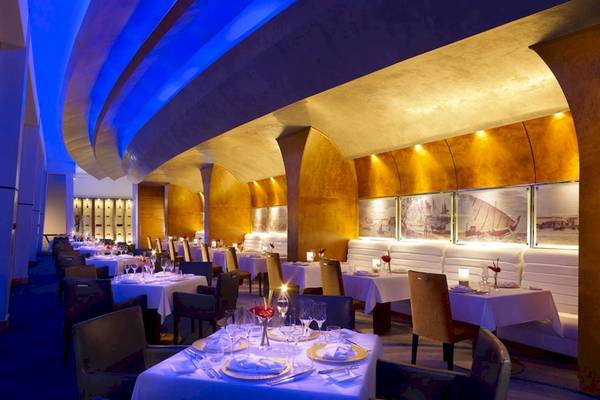 Innenbereich des Shangri-La Al Husn Resorts & Spa, mit blauen Lichtern und goldenen Wänden, gedeckten Tischen und Stühlen.