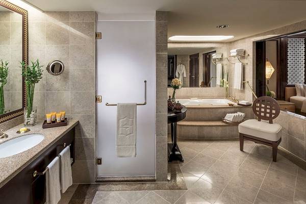 Luxuriöses Badezimmer im Shangri-La Al Husn Resort & Spa mit Badewanne, Dusche, Spiegel und Holzstuhl.