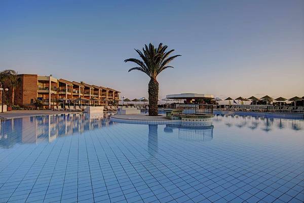 Außenpool des Candia Maris Resort & Spa mit Palme und Gebäude im Hintergrund.