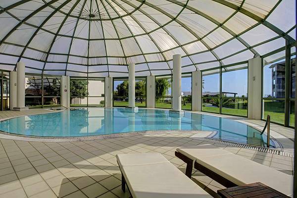 Innenpool des Candia Maris Resort & Spa mit Glasdach und weißen Fliesenboden.