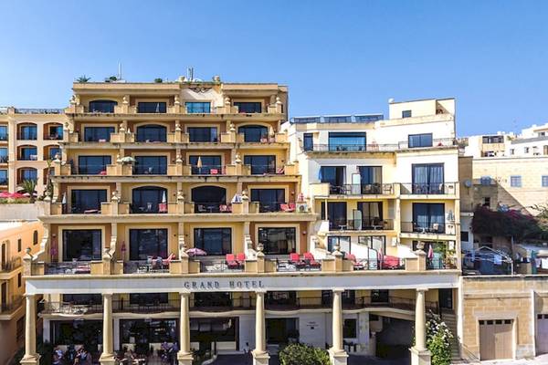 Außenansicht des Grand Hotel Gozo mit mehreren Stockwerken, Balkonen und Gästebereichen.