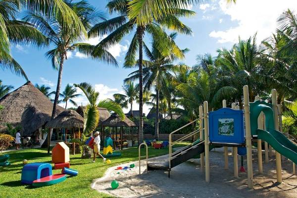 Kinderspielplatz im Freien im La Pirogue Mauritius Hotel, umgeben von Palmen und Strohhütten.