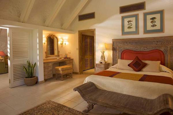 Innenansicht eines Schlafzimmers im La Pirogue Mauritius Hotel mit einem großen Bett, Kopfteil, Nachttischen und dekorativen Elementen.