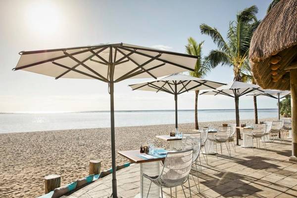 Strandrestaurant von La Pirogue Mauritius mit Tischen und Stühlen unter Schirmen.