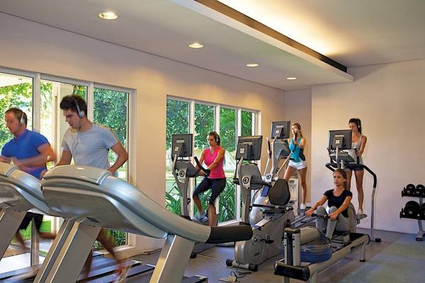 Fitnessraum im La Pirogue Mauritius Hotel mit mehreren Personen, die auf verschiedenen Trainingsgeräten trainieren.