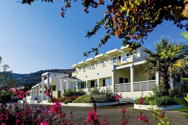 Außenansicht des Lindos White Hotel & Suites mit weißen Gebäuden, Balkonen und umgeben von Pflanzen und Blumen.