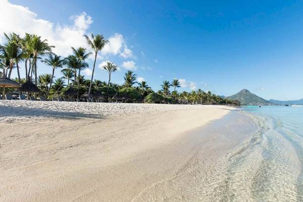 Strand des La Pirogue Mauritius Hotels mit weißen Palmen und blauem Wasser