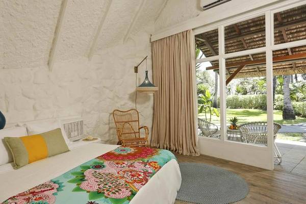 Schlafzimmer im La Pirogue Mauritius Hotel mit farbenfroher Bettdecke, weißen Wänden und Gartenblick.