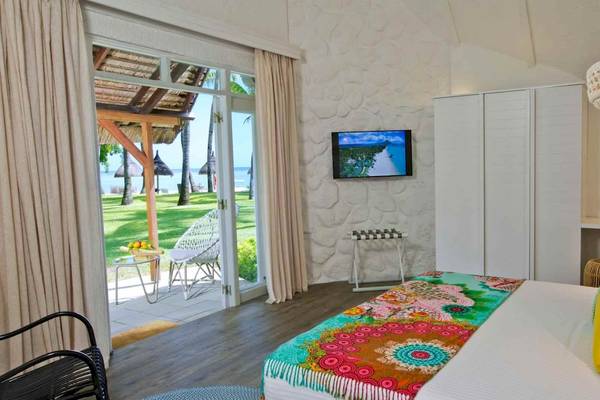 Innenansicht eines Zimmers im La Pirogue Mauritius Hotel mit einem großen Bett, Fernseher und Glastür zum Balkon.