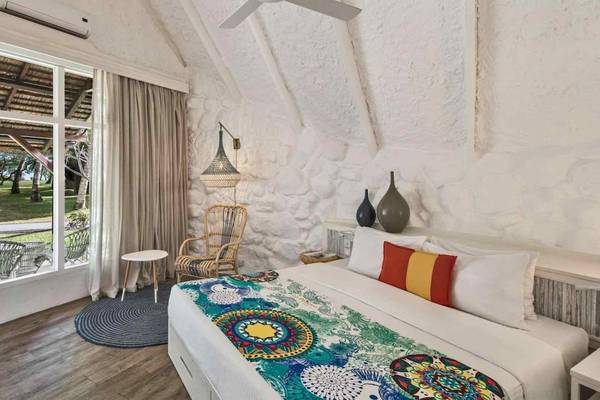 Innenansicht eines Zimmers im La Pirogue Mauritius Hotel mit weißem Bett, Holzboden und Glastür.