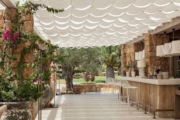 Terrasse des Sani Clubs mit Bar, weißen Stühlen und Steinwänden.