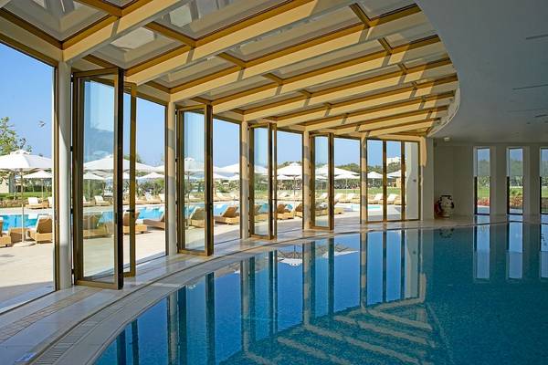 Innenansicht des Pools im Sani Club Hotel mit großen Glastüren und Sonnenliegen.